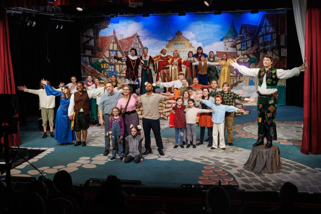 The full cast of Piper: A New Musical stands on stage at KMC Onstage performing the finale with arms outstretched.